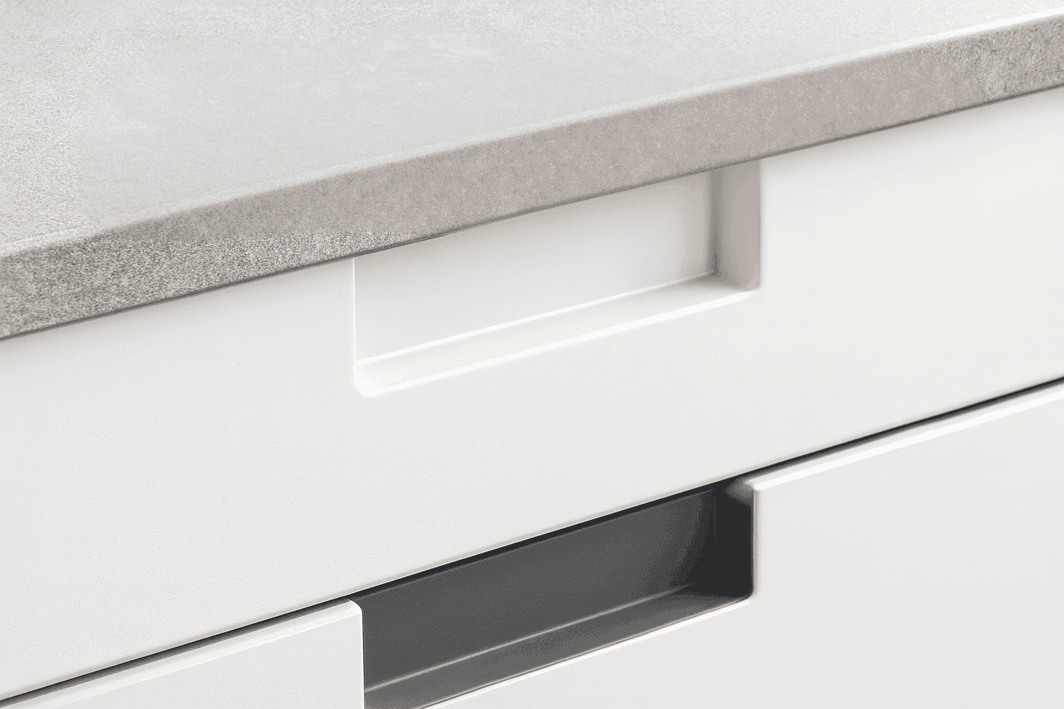 Weiße grifflose Küchenschublade mit integrierter Griffmulde unter grauer Arbeitsplatte in moderner Küchenumgebung.