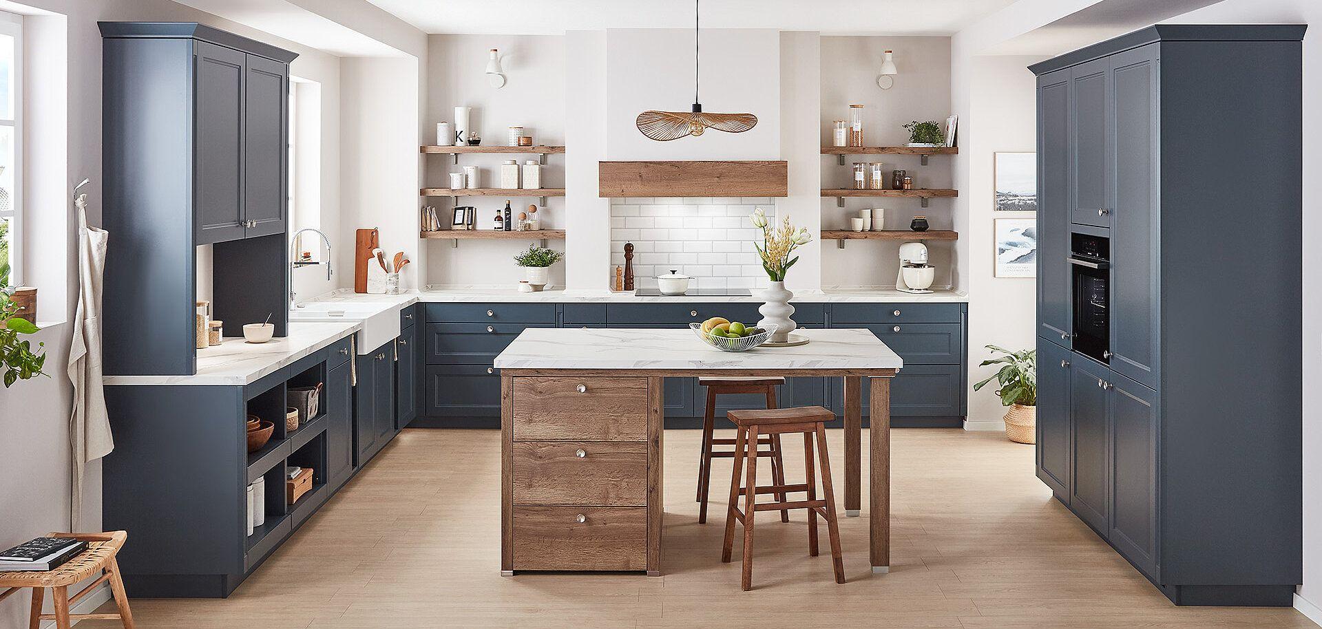 Landhausküche mit blauen Rahmenfronten, Knopfgriffen und Kochinsel aus Holz mit weißer Arbeitsplatte.